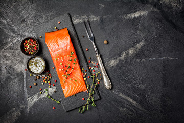 Piece of red fish fillet with spices on black slate board with vintage silver fork