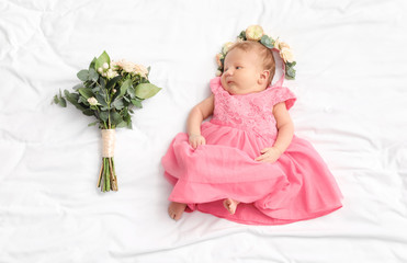 Cute little baby girl with beautiful flowers lying on bed