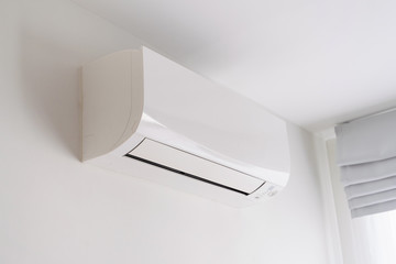 Air conditioner on white concrete wall in area of room.