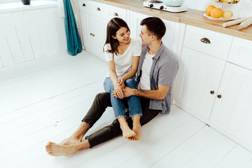 Full-length image of romantic couple at home. Attractive young woman and handsome man are enjoying spending time together while standing on light modern kitchen.