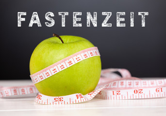 green apple with tape measure with black background and german text fastenzeit, in english fasting...