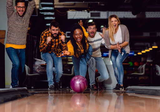 Group of friends enjoying time together laughing and cheering while bowling at club.