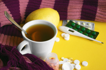 Cup of tea with lemon with pills and a thermometer on a yellow background.