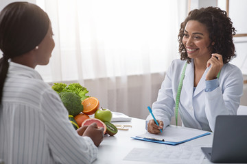 Smiling black woman talking to female patient, taking notes
