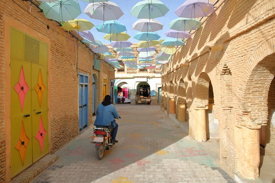 Typical cobbled and narrow street  inside the medina of Nefta, Tunisia, with colorful umbrellas and doors 
