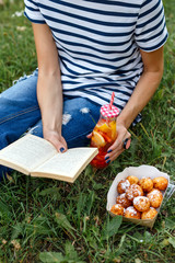 The girl is resting in nature, eating donuts, reading a book, water in a bottle with fruit