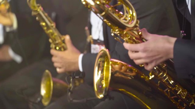 Close-up of musicians playing saxophones at concert. Action. Beautiful musicians in costumes play golden saxophones during city holiday concert