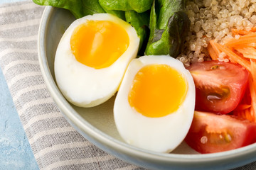 Healthy green vegetarian buddha bowl lunch with eggs, quinoa, carrots,tomato, lettuce leaves, on a blue background., close up