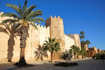 The impressive ramparts of the medina surrounded by colorful palmtrees and a large cobbled walkway...