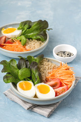 Healthy green vegetarian buddha bowl lunch with eggs, quinoa, carrots,tomato, lettuce leaves, on a blue background.