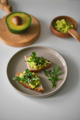 Toast with avocado, arugula on a plate and avocado or wooden board in the shape of deer antlers. Bowl with guacamole