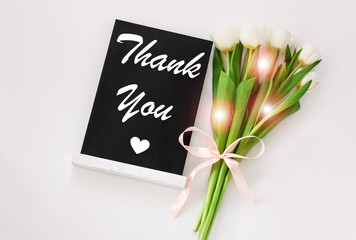 Thank You card message sign on black chalkboard with tulip flowers on white background flat lay.Blackboard greeting text