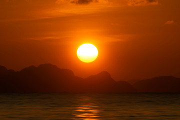 Big sun on sunset sky at the lake with silhouette mountain