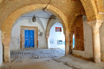Naklejka premium Typical cobbled and narrow street with colorful doors, columns and arcades inside the historical medina of Tunis, Tunisia