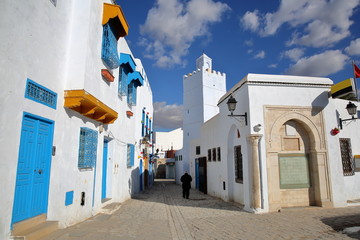 Typical whitewashed houses and cobbled streets, located inside the medina of Kairouan, Tunisia, with the white minaret of Khayroun Mosque in the background