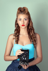 A pretty pin-up girl with a vintage camera on a soft green background.