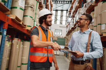 Happy handsome customer in formal clothing shaking hand of factory manager with clipboard after...