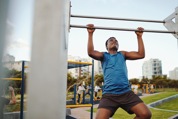 Fototapeta na wymiar Front view of a strong african american male athlete doing pull-up on horizontal bar in the public gym park