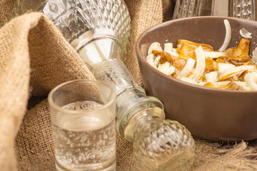 Salted mushrooms with onions in a ceramic bowl, a decanter and a glass of vodka on a background of...