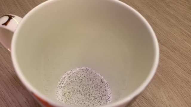 Putting cappuccino powder into a white cup with a spoon. Closeup of white and brown instant coffee particles in a ceramic cup. Making instant capuccino.
