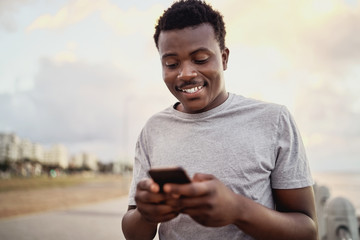 Portrait of a happy athlete young man texting messages on smart phone standing against the city background