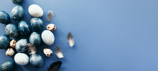 Beautiful group ombre blue Easter eggs with quail eggs and feathers on a blue background. Easter concept. Border eggs. Copy space for text
