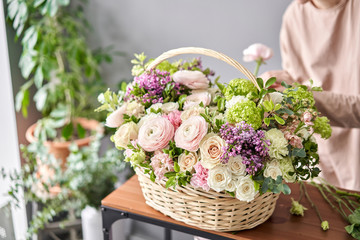 Floral shop concept . Florist woman creates flower arrangement in a wicker basket. Beautiful...