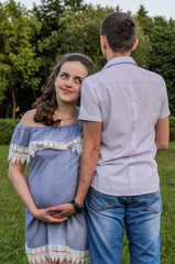 Fototapeta premium Young couple in love on a walk in the park, husband hugs pregnant wife by the belly, happy family