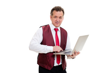 Naklejka na ściany i meble Portrait of happy businessman senior 60-65 years old in marsala vest with red tie and laptop in hands. he has a smart look on white isolated background. facial expression