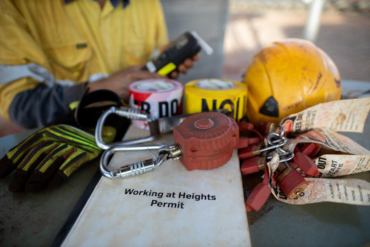 Working At Heights Permit Book Placing On The Table An Inertia Reel Shock Absorbing Fall Protection Device Danger Caution Tags Hard Hat Safety Glove And Worker Holding Alcohol Tester At The Background