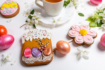 Close-up Easter festive gingerbreads and colored eggs with cup of tea and white Apple tree twigs on white background.