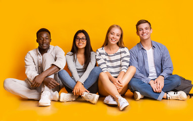 Happy students posing over yellow studio background