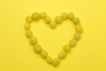 The concept of minimalism. Heart made of sweet yellow sweets on a bright yellow background. top view.