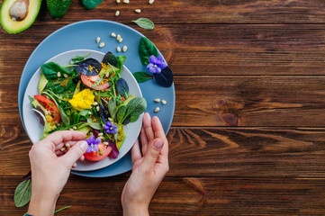 Young woman preparing fresh healthy salad with edible flowers on wooden background with blank space