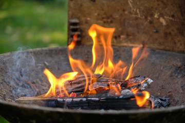 Flames coming out of a heap of cardboard, paper, wood and twigs in a barbecue in the garden.
