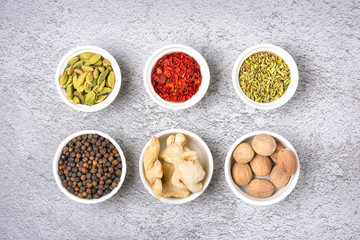 mix of aromatic spices coriander, black pepper, bergamot, dried ginger, nutmeg, paprika in white cups on gray concrete background Top view Flat lay Healthy food