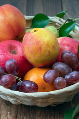 red grape berries and fresh fruits in a straw basket on a dark wooden background.