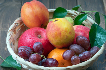 red grape berries and fresh fruits in a straw basket on a dark wooden background.