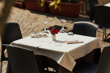 Beautiful decorations of table in open air. Close up view of restaurant table with romantic place setting with red flowers, plates, cutlery on white background. Romantic dinner.