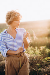 Free beautiful woman with curly hair in a field with wheat with a spikelet in the hands at sunset. Female power and independence. Soft selective focus.