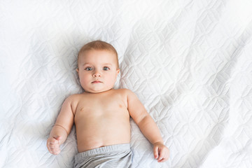 Portrait of a cute baby of nine months. A small boy watches with interest what is happening on the bed White background with copy space