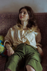 Fototapeta premium .Beautiful girl in green pants sits on a sofa.
