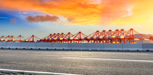 Empty asphalt highway and industrial container freight port at beautiful sunset in Shanghai.