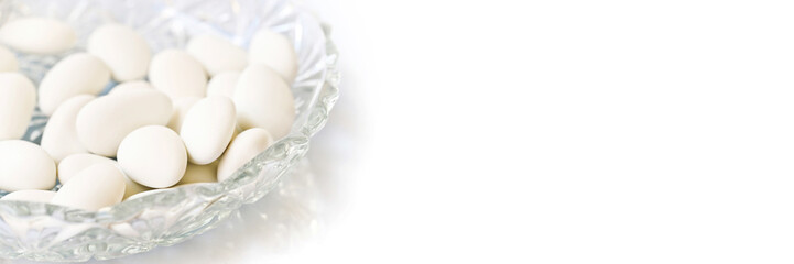 White dragees in a plate for baptism or wedding on white panoramic background