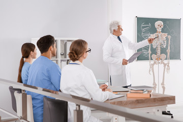 Obraz premium Medical students and professor studying human skeleton anatomy in classroom