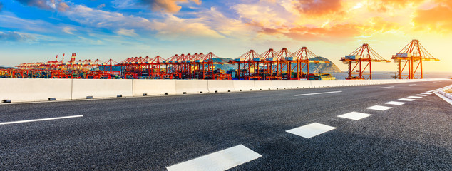 Empty asphalt highway and industrial container freight port at beautiful sunset in Shanghai.