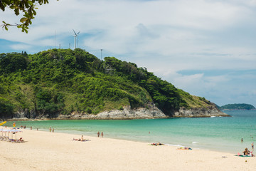 Phuket, Thailand - April 19, 2017. Sea beach with people and umbrellas, a large green hill and a wind generator.