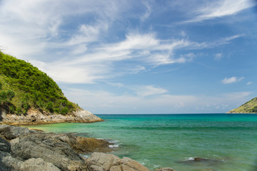 Turquoise sea with a horizon line, two green hills and large stones in the foreground.