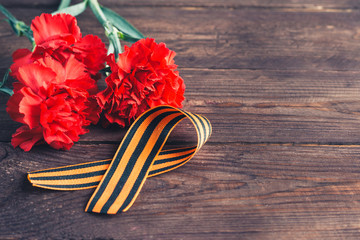 Georgievsk ribbon - Russian symbol of victory and three red carnations on a dark wooden background....