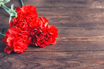 Three red carnations on a dark wooden background. Holiday card for the holiday of May 9.